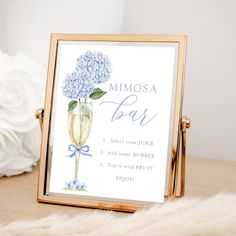 a blue hydrangea flower in a champagne glass is displayed on a gold frame