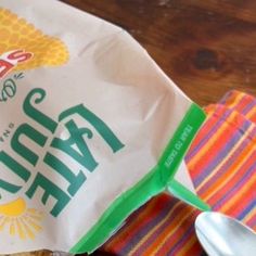 a bag of chips sitting on top of a wooden table next to a cup and spoon