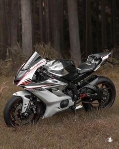 a silver and black motorcycle parked on top of a grass covered field next to trees