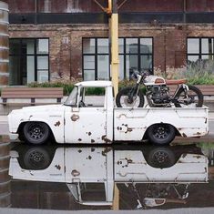 an old pickup truck with a motorcycle on the back parked in front of a building