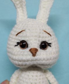 a crocheted white stuffed animal with brown eyes and ears, sitting on a blue background