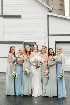 a group of women standing next to each other in front of a white building holding bouquets