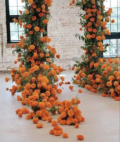 an arrangement of orange flowers on the ground in front of two large windows with brick walls