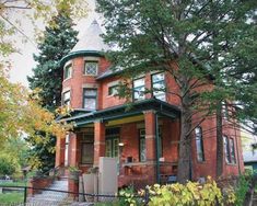 a red brick house with a green roof and trees in the front yard, surrounded by greenery