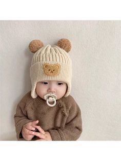 a baby wearing a knitted bear hat and pacifier