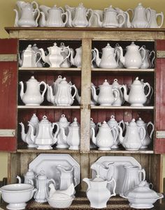 an old china cabinet filled with white dishes and teapots on top of wooden shelves