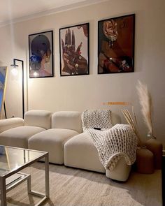 a living room with white couches and pictures on the wall above them in front of a coffee table