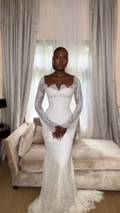 a woman standing in front of a couch wearing a white wedding dress with long sleeves