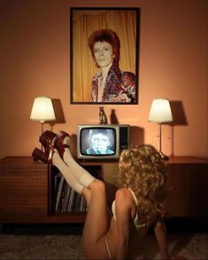 a woman sitting on the floor in front of a tv with her feet up to a lamp