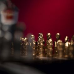 a chess board with gold pieces on it and a red wall in the back ground