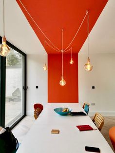 an orange and white dining room with lights hanging from the ceiling over the long table