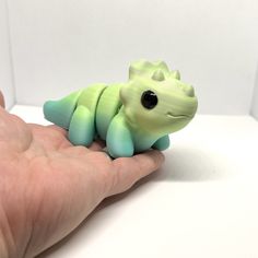 a small green toy sitting on top of a person's hand in front of a white wall