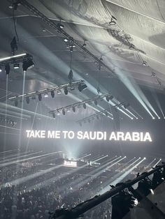 the words take me to saudi are lit up in front of an audience at a concert