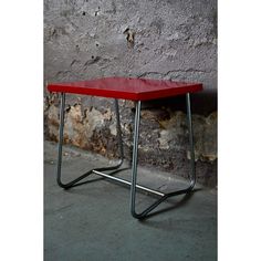 a red table sitting on top of a metal frame next to a brick wall and cement floor