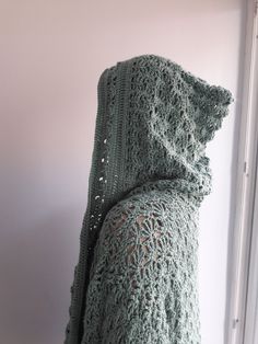 a green crocheted shawl draped over a window sill in front of a white wall