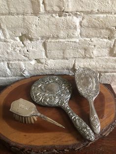 three silver spoons sitting on top of a piece of wood next to a brush