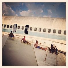 four people sitting on the ground in front of an airplane