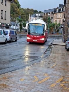 a red and white bus driving down a street next to tall buildings on a rainy day