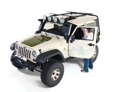 a man standing next to a white jeep with its hood up and lights on, in front of a white background