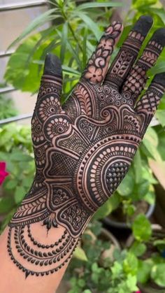 a hand with henna on it in front of some plants and flowers, the image is