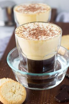 two cups filled with hot chocolate and topped with whipped cream on a wooden tray next to cookies