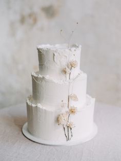 a three tiered white cake with flowers on the top and bottom, sitting on a table