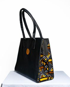 Stunning Top Leather Handle  / Dashiki print women's handbag made with a beautiful Ankara print on the sides and black leather. The fabric design is a modern rendition of a classic wax print motif. The simple geometric shape of the bag goes well with most contemporary ensembles. The bag is beautifully handcrafted and features two interior zippered pockets Primary color: BLACK Materials: Ankara cloth, Metalic zip enclosure, Leather Length: - 16.5 Inches Height:- 14 Inches Width :- 6 Inches Foam padded to protect your electrical gadgets, hence great as a work bag with ones laptop or tablet. This is a fancy and classy bag that can be used to carry your gadgets safely.  Its best for carrying most of your essentials ! African Print Bags Handbags, Black Square Box Bag With Leather Handles, Black Square Satchel With Leather Handles, Black Box Bag With Double Leather Handles, Black Double Handle Box Bag With Leather Handles, Electrical Gadgets, Ankara Bags, Laptop Pouch, Unique Handbags