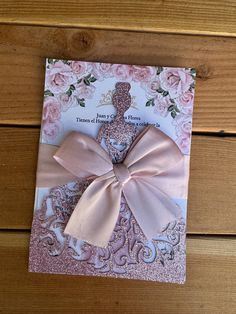 a card with a pink bow on top of it next to a wooden table and wood planks