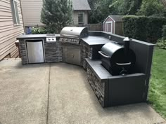 an outdoor kitchen with grills and sink in the middle of a driveway area next to a house