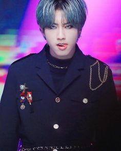 a man with blue hair wearing a black jacket and silver chain around his waist is looking at the camera