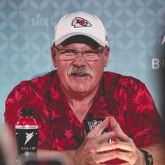 a man in a red shirt and white hat sitting at a table with two beer bottles