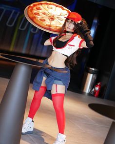 a woman holding a pizza on top of her head while standing next to a pole