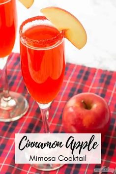 two wine glasses filled with cinnamon apple mimosa cocktail next to an apple on a checkered tablecloth