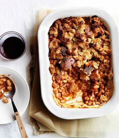 a casserole dish with meat and beans in it next to two cups of coffee