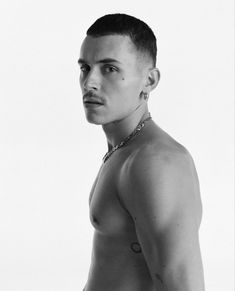 black and white photograph of a shirtless man wearing a chain around his neck, looking at the camera