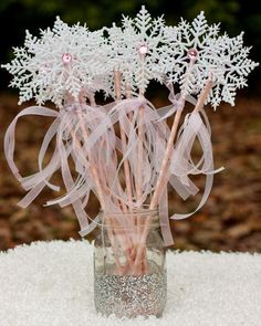 a glass vase filled with snowflakes and pink ribbon on top of a table