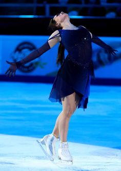 a female figure skating on the ice in a black dress and white tennis shoes with her arms outstretched