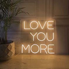 a neon sign that says love you more on it next to a potted plant