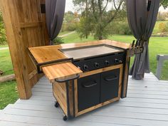 an outdoor bbq grill sitting on top of a wooden deck next to a green field