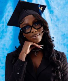 a woman wearing glasses and a graduation cap is posing for a photo in front of a blue backdrop