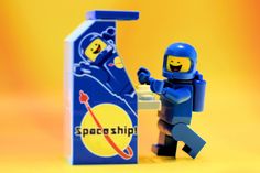 a lego man standing next to a blue space ship box with the word space shuttle on it