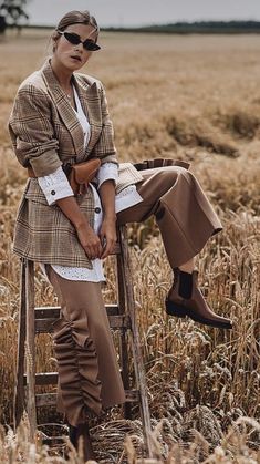 a woman sitting on top of a wooden chair in a field