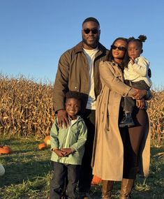 a man, woman and child standing in front of a cornfield with pumpkins