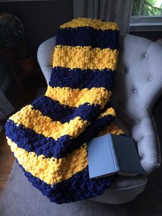 a blue and yellow crocheted blanket sitting on top of a chair next to a book