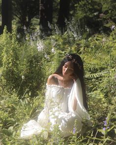 a woman is sitting in the grass with her arms around her neck and wearing a white dress