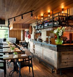 an empty restaurant with wooden tables and chairs, bottles on the wall behind the bar