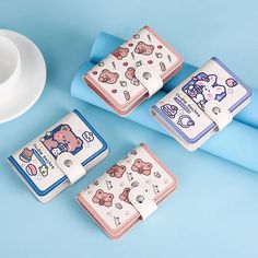 four hello kitty wallets sitting next to each other on a blue surface with a cup and saucer