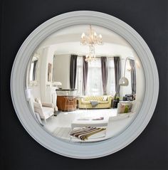 a mirror reflecting a living room and dining room with couches, chairs, chandelier