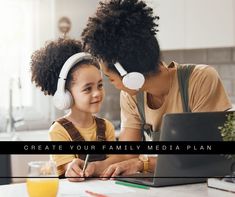 a woman and child sitting at a table with headphones on looking at a laptop