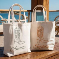 two personalized tote bags sitting on top of a wooden table next to the ocean